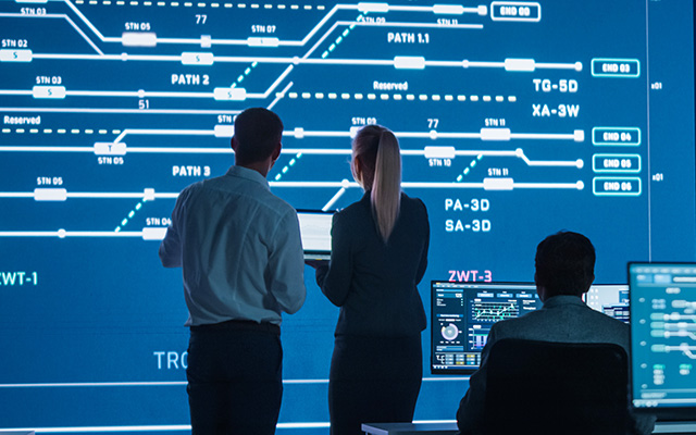 Control room operators standing in front of an LED videowall showing telecoms data